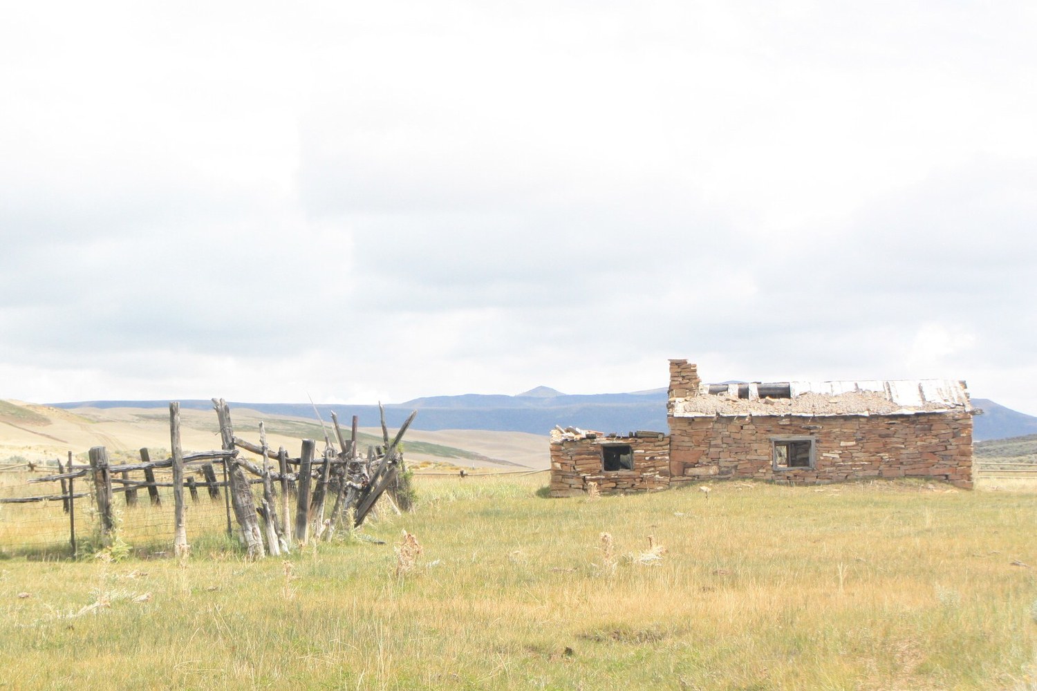 A stone ranch ruin and a fallen corral fence on the open sagebrush range.